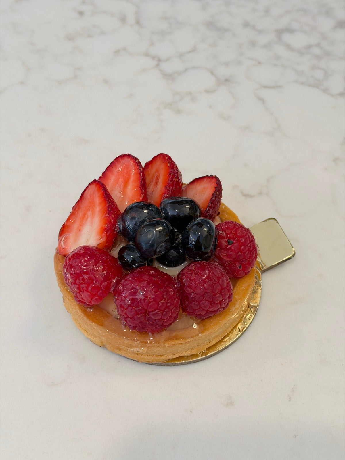 An individual Le 76 fresh fruit tart with strawberries, raspberries and blueberries