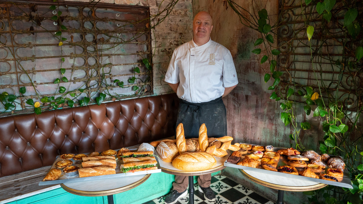 Jean-Marc Masset in his chef's whites behind three marble tables holding the day's baguettes, pastries and sandwiches at Le 76