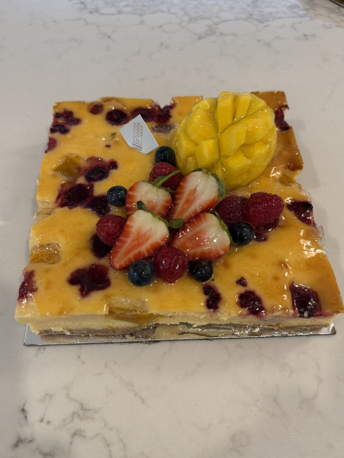 A whole Le 76 baked cheesecake topped with mango and fresh berries
