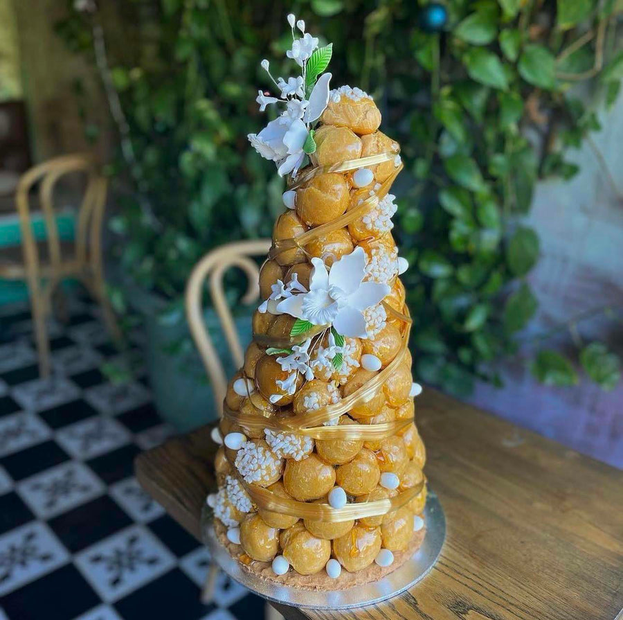 A tall Le 76 croque en bouche, caramel glazed choux bound in spun sugar and dressed with white blossom