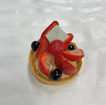 An individual Le 76 fruit tartlet with strawberries and blueberries on crème pâtissière, with the Le 76 tag