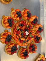A tray of Le 76 fruit tartlets topped with strawberries and blackberries, arranged around a larger fruit tart