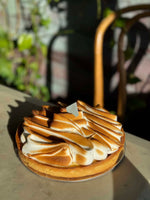 A whole Le 76 lemon meringue tart on the counter, the meringue piped in wide sweeps and torched