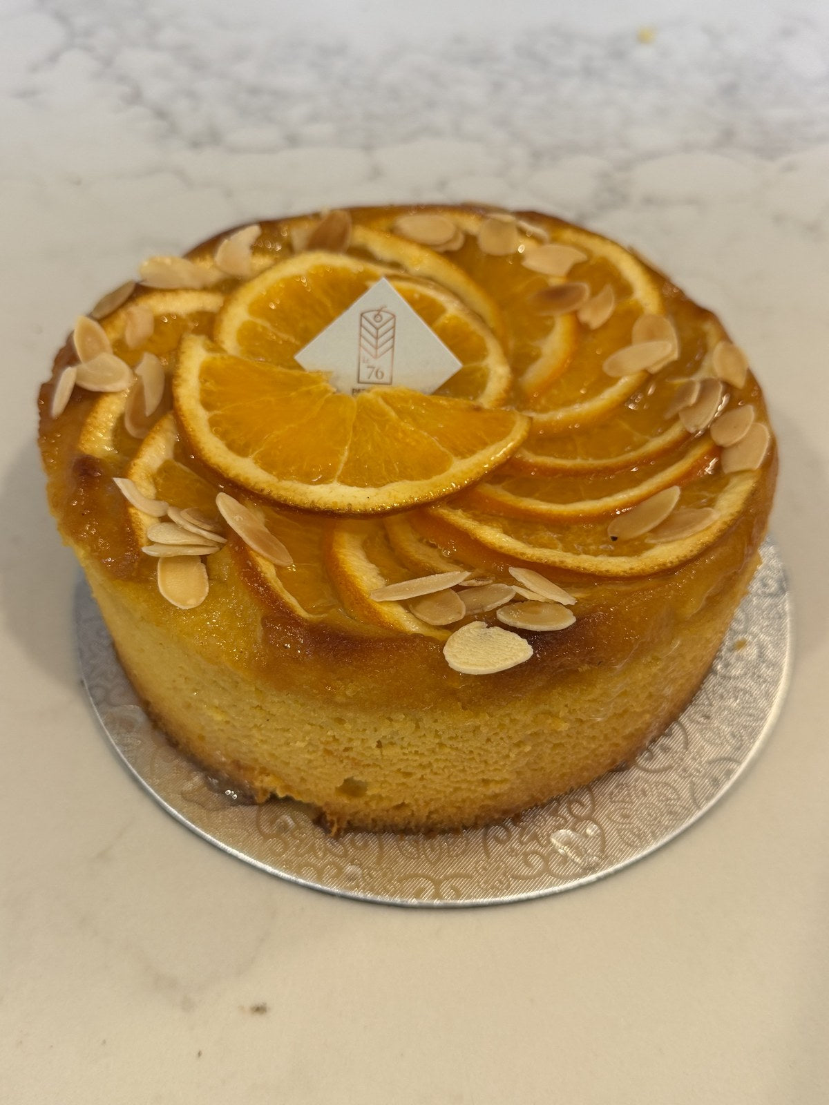 A whole Le 76 orange and almond cake, gluten and dairy free, topped with orange slices