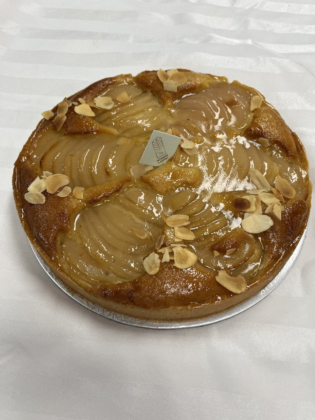 A whole Le 76 pear and almond tart, pear halves fanned across the top with flaked almonds