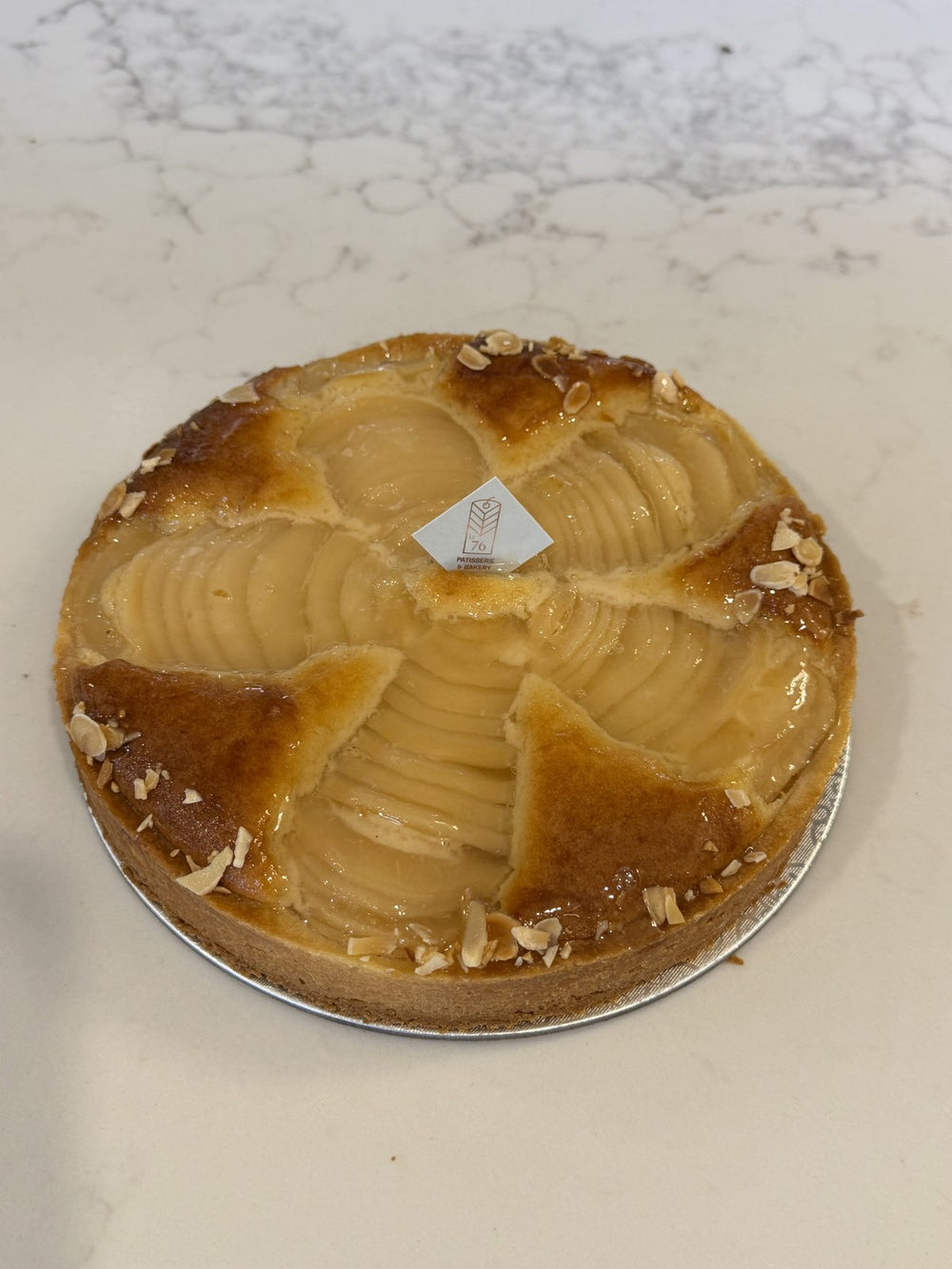 A whole Le 76 pear and almond tart, pear halves fanned in frangipane with flaked almonds