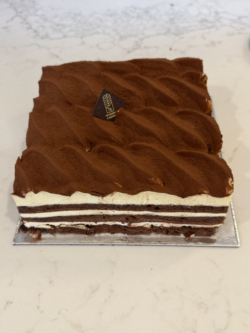 A whole Le 76 tiramisu, layered savoiardi and mascarpone finished with cocoa