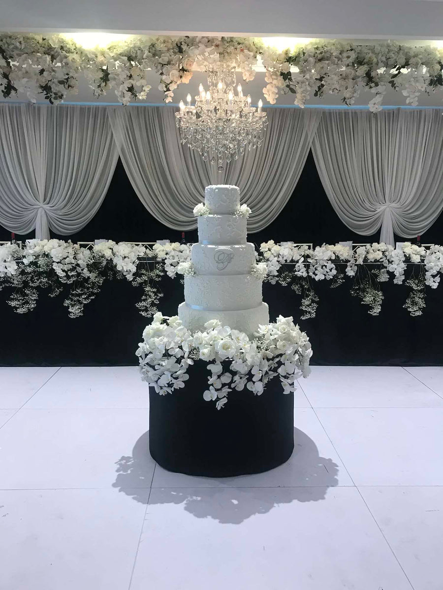 A tiered celebration cake by Le 76 in black and white, finished with cascading white blossom