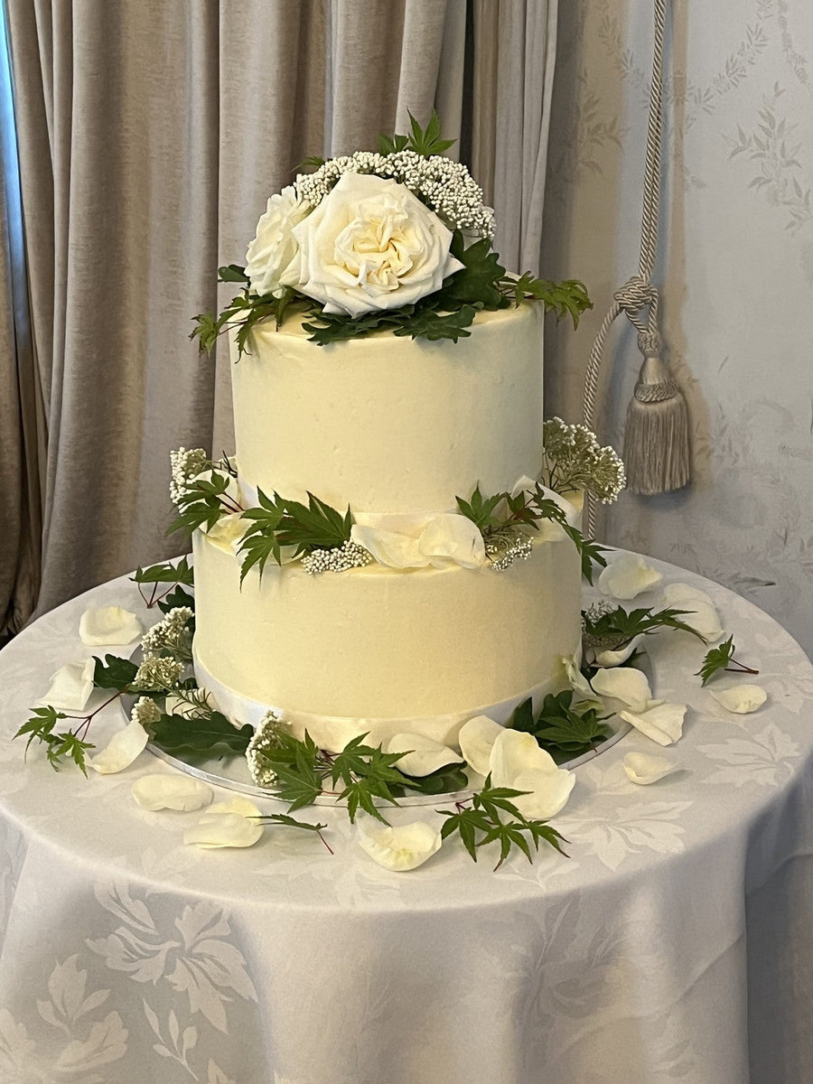 A two tier Le 76 wedding cake finished with white roses and foliage