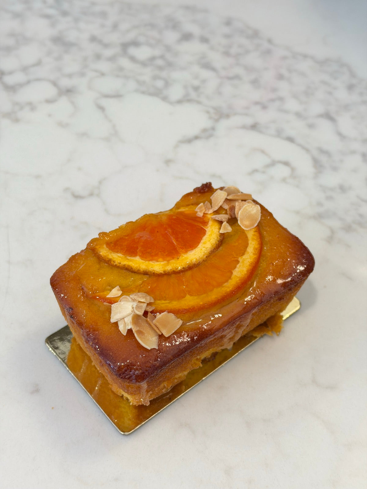 An individual Le 76 orange and almond cake, gluten and dairy free, topped with orange